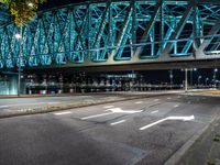 an empty city road in front of an illuminated bridge at night on a street corner