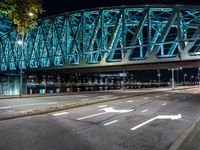 an empty city road in front of an illuminated bridge at night on a street corner