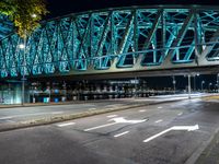 an empty city road in front of an illuminated bridge at night on a street corner