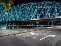 an empty city road in front of an illuminated bridge at night on a street corner