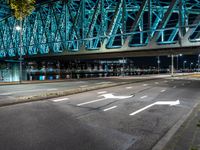 an empty city road in front of an illuminated bridge at night on a street corner