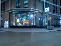 a lighted store sits outside a brown brick building in a city at night with no traffic