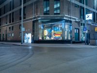 a lighted store sits outside a brown brick building in a city at night with no traffic