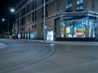 a lighted store sits outside a brown brick building in a city at night with no traffic