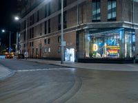 a lighted store sits outside a brown brick building in a city at night with no traffic