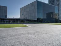 an intersection in the middle of an empty lot on a bright, sunny day with the windows of a large modern building reflecting the sky