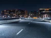 there are two lanes on the bridge that is lit up at night with buildings and a dark sky above