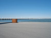 a view of a pier with a metal structure overlooking the water and a sail boat in the distance