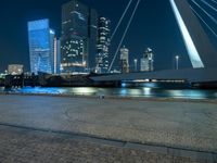 a woman is walking down the sidewalk by the water at night with city lights in the background