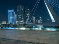 a woman is walking down the sidewalk by the water at night with city lights in the background