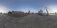 a fisheye lens of a street, water and a bridge in the distance, with buildings near the water