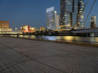 a river runs through a city near tall buildings and some benches in the foreground