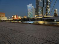 a river runs through a city near tall buildings and some benches in the foreground