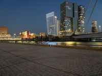 a river runs through a city near tall buildings and some benches in the foreground