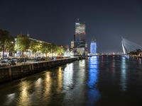 an illuminated bridge is seen across a river at night next to large buildings and lights