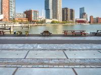 several benches along the water with buildings in the background of the picture of a city with water