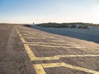 yellow lines on asphalt by sand and hills during sunrise as a vehicle travels away from a car