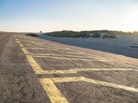 yellow lines on asphalt by sand and hills during sunrise as a vehicle travels away from a car