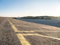 yellow lines on asphalt by sand and hills during sunrise as a vehicle travels away from a car