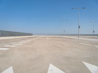 a parking lot filled with lots of empty concrete areas under blue skies and a line of street lamps