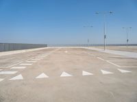 a parking lot filled with lots of empty concrete areas under blue skies and a line of street lamps