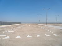 a parking lot filled with lots of empty concrete areas under blue skies and a line of street lamps