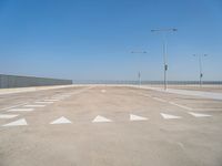 a parking lot filled with lots of empty concrete areas under blue skies and a line of street lamps