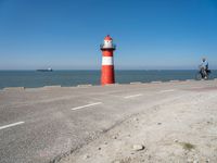 a man on a bike near the ocean by the water with a lighthouse at the edge