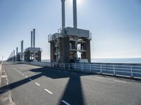 a bridge over the ocean with construction equipment in the background and two people walking on it