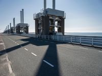 a bridge over the ocean with construction equipment in the background and two people walking on it