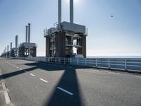 a bridge over the ocean with construction equipment in the background and two people walking on it