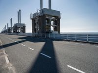 a bridge over the ocean with construction equipment in the background and two people walking on it