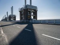 a bridge over the ocean with construction equipment in the background and two people walking on it