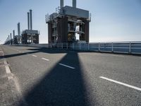 a bridge over the ocean with construction equipment in the background and two people walking on it