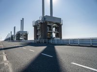 a bridge over the ocean with construction equipment in the background and two people walking on it