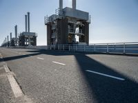 a bridge over the ocean with construction equipment in the background and two people walking on it