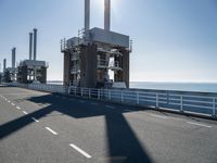 a bridge over the ocean with construction equipment in the background and two people walking on it