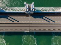 a bridge over the ocean with construction equipment in the background and two people walking on it