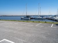 a parking lot filled with parked boats next to a lake and body of water with small boats docked in the background