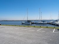 a parking lot filled with parked boats next to a lake and body of water with small boats docked in the background