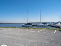 a parking lot filled with parked boats next to a lake and body of water with small boats docked in the background