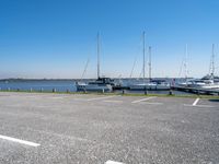 a parking lot filled with parked boats next to a lake and body of water with small boats docked in the background