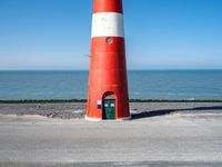 the red and white lighthouse sits on the concrete ground near the ocean area for the picture