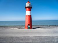 the red and white lighthouse sits on the concrete ground near the ocean area for the picture