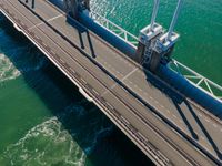 a bridge over the ocean with construction equipment in the background and two people walking on it