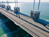 a bridge over the ocean with construction equipment in the background and two people walking on it