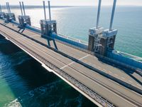 a bridge over the ocean with construction equipment in the background and two people walking on it