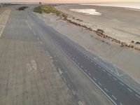 an aerial view of the desert road running on sand, overlooking the ocean and a sandy beach