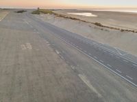 an aerial view of the desert road running on sand, overlooking the ocean and a sandy beach