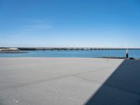 an empty beach with the sea and bridge in the back ground behind it, which are also a few small docks